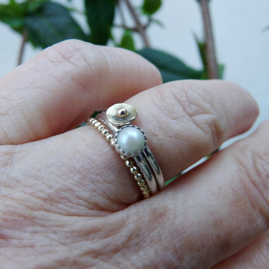 Hand met gedragen stapelringen set Zonlicht van zilver en 14k goud met parel.