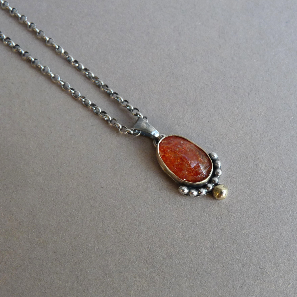 Bicolor ketting van goud en zilver met een facetgeslepen zonnesteen hanger liggend op een grijze achtergrond
