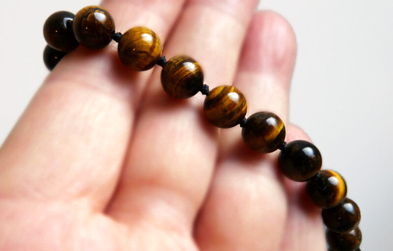 Close-up of the hand-knotted tiger eye necklace for men held in a hand to show the shine and texture of the natural gemstone beads