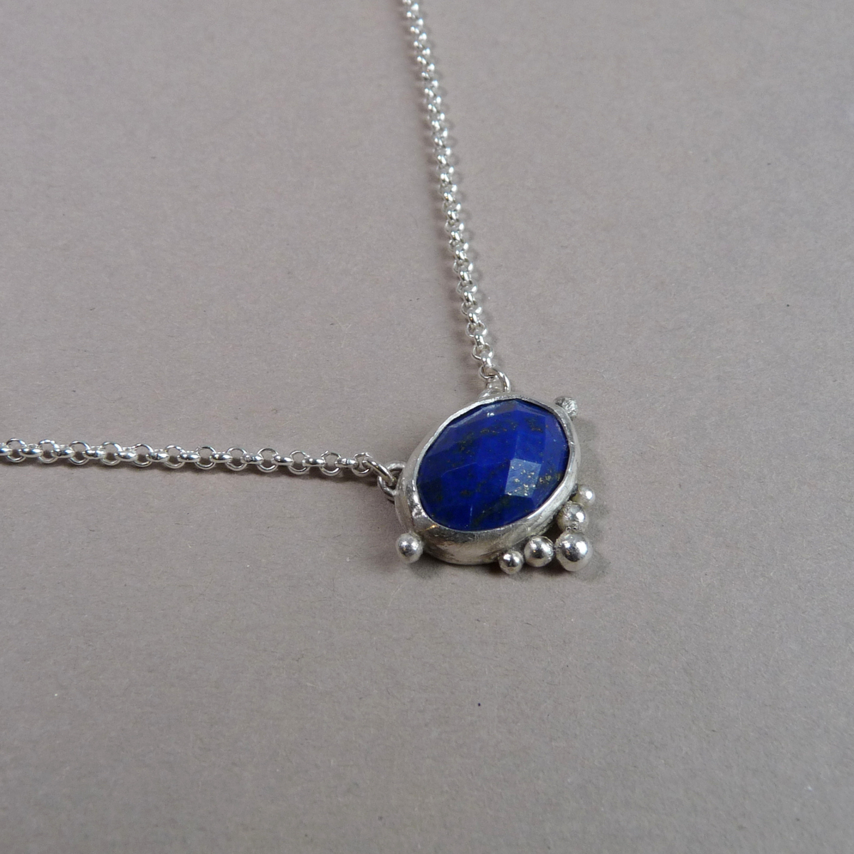 Close-up van de handgemaakte zilveren hanger met een facetgeslepen blauwe lapis lazuli edelsteen en verfijnde granules