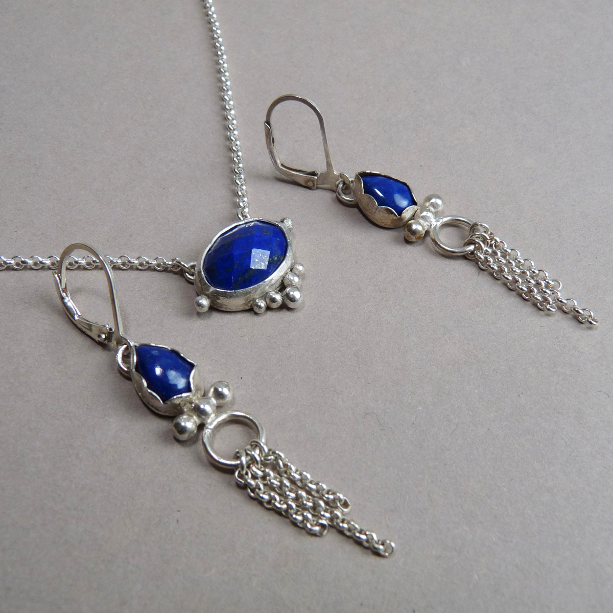 De facetgeslepen lapis lazuli edelsteen ketting liggend gefotografeerd samen met de bijpassende zilveren hangende oorbellen met kettinkjes