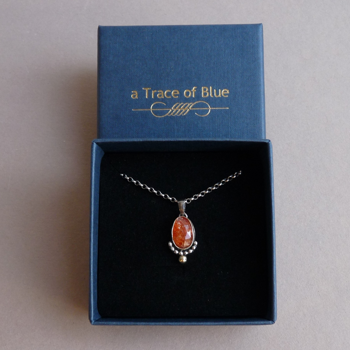 De bicolor zonnesteen hanger ketting gepresenteerd in een luxe donkerblauw sieradendoosje van aTraceof Blue
