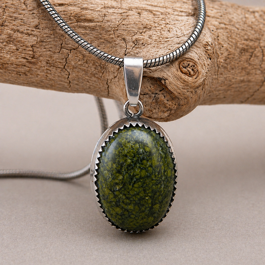 Close-up van een handgemaakte zilveren herenketting met een ovale groene serpentijn edelsteen op hout