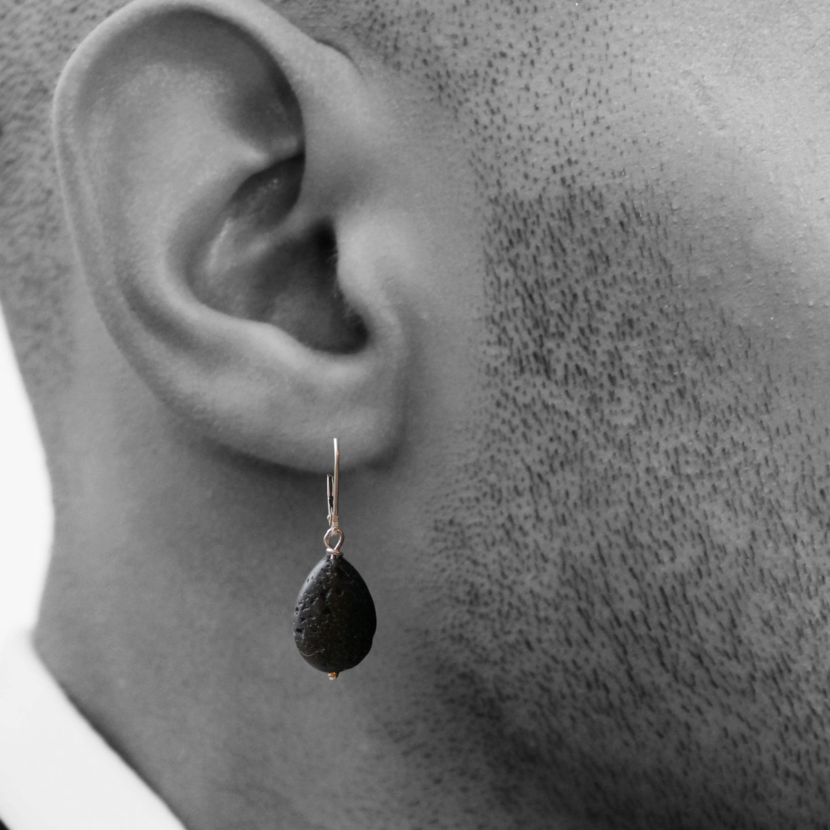 Mannelijk model draagt een handgemaakte zilveren heren oorbel met een matte zwarte lava druppel